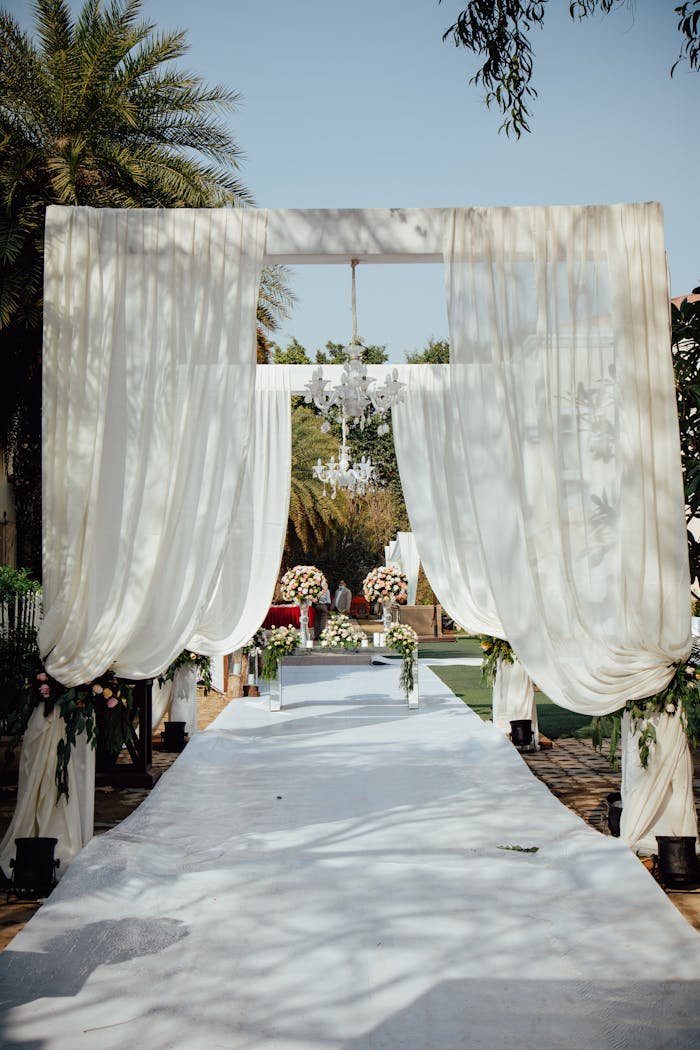 our-experience A beautifully decorated outdoor wedding aisle with draped curtains and floral arrangements, set for a ceremony.