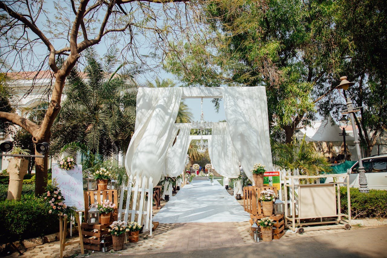 Beautiful outdoor wedding archway decorated with white drapes and flowers surrounded by trees.